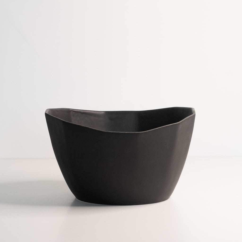 Empty medium porcelain bowl in Mica Black, its soft wavy rim rising over faceted sides on white