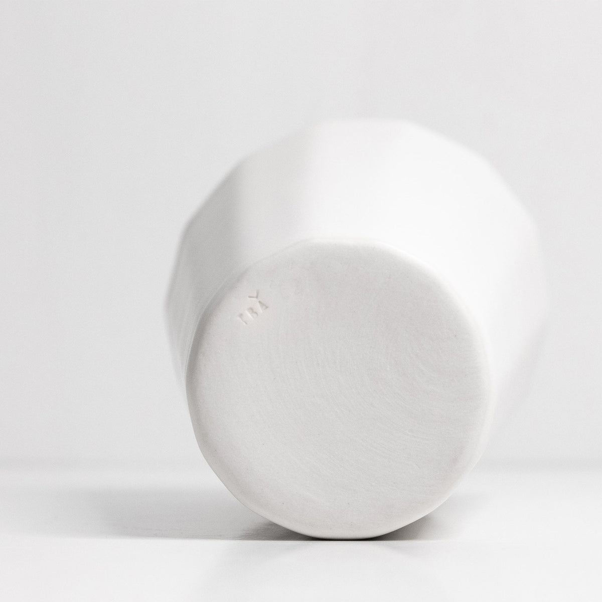 Underside of a white porcelain pint cup showing its faceted body and smooth unglazed base
