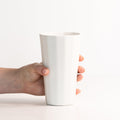 Hand holding a tall Silk White porcelain pint cup to show its height and tapered faceted body