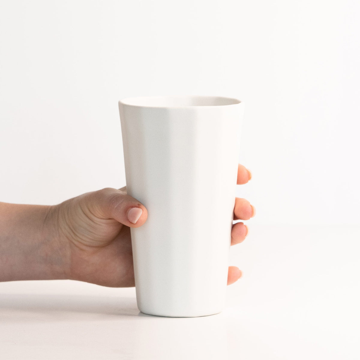 Hand holding a tall Silk White porcelain pint cup to show its height and tapered faceted body