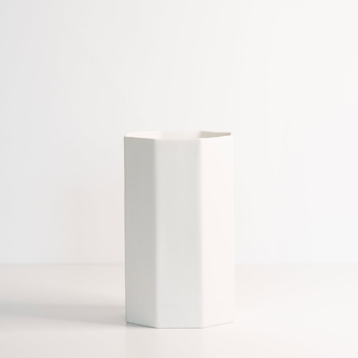 Empty tall octagonal porcelain vase in Silk White on a white surface, showing its clean flat facets