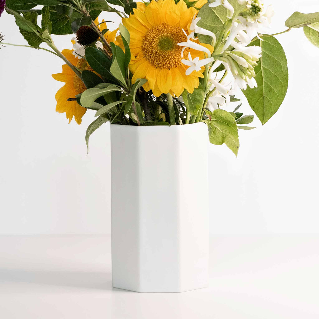 Tall octagonal porcelain vase in Silk White filled with sunflowers and leafy summer greens on white