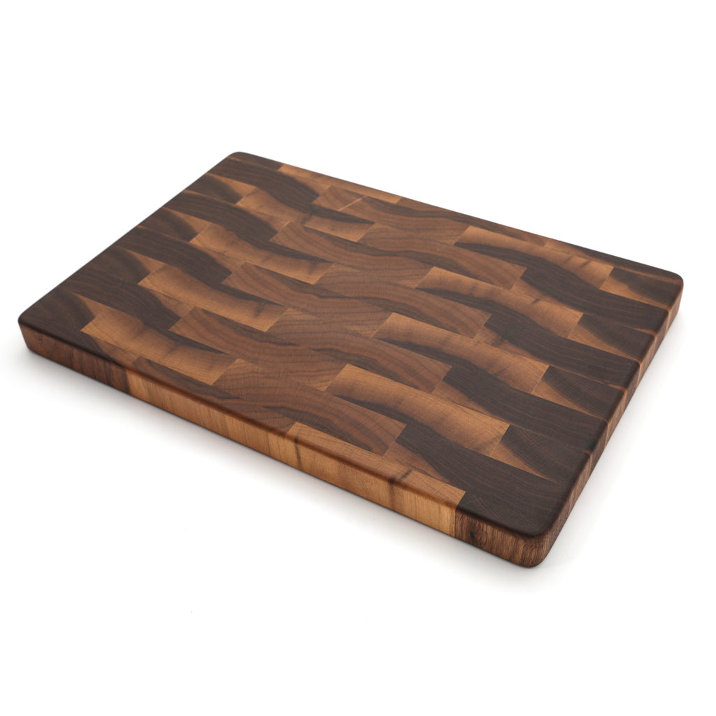 End grain walnut cutting board, 18 x 12 in, lying at an angle on white with a dark brick pattern