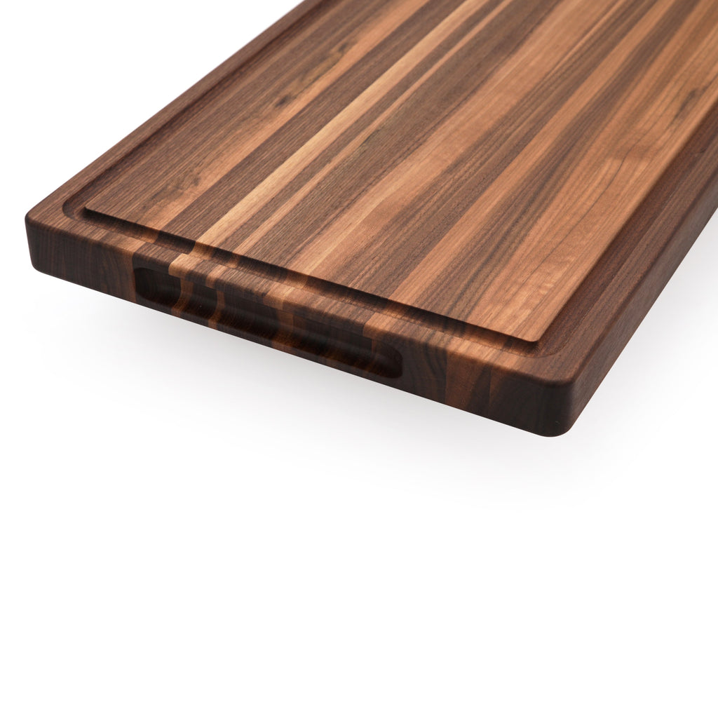 Close view of an edge grain walnut cutting board corner with a juice groove and pocket handle below
