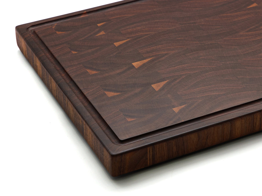Corner close-up of an end grain walnut cutting board showing the juice groove and pale wood flecks