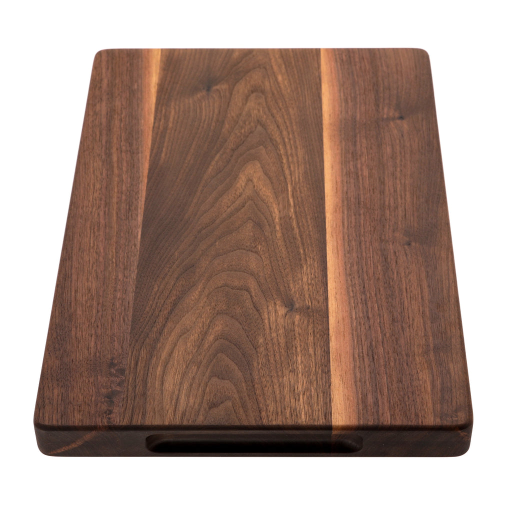 Thick walnut cutting board, 18 x 12 in, seen end-on with the carved side handle visible underneath
