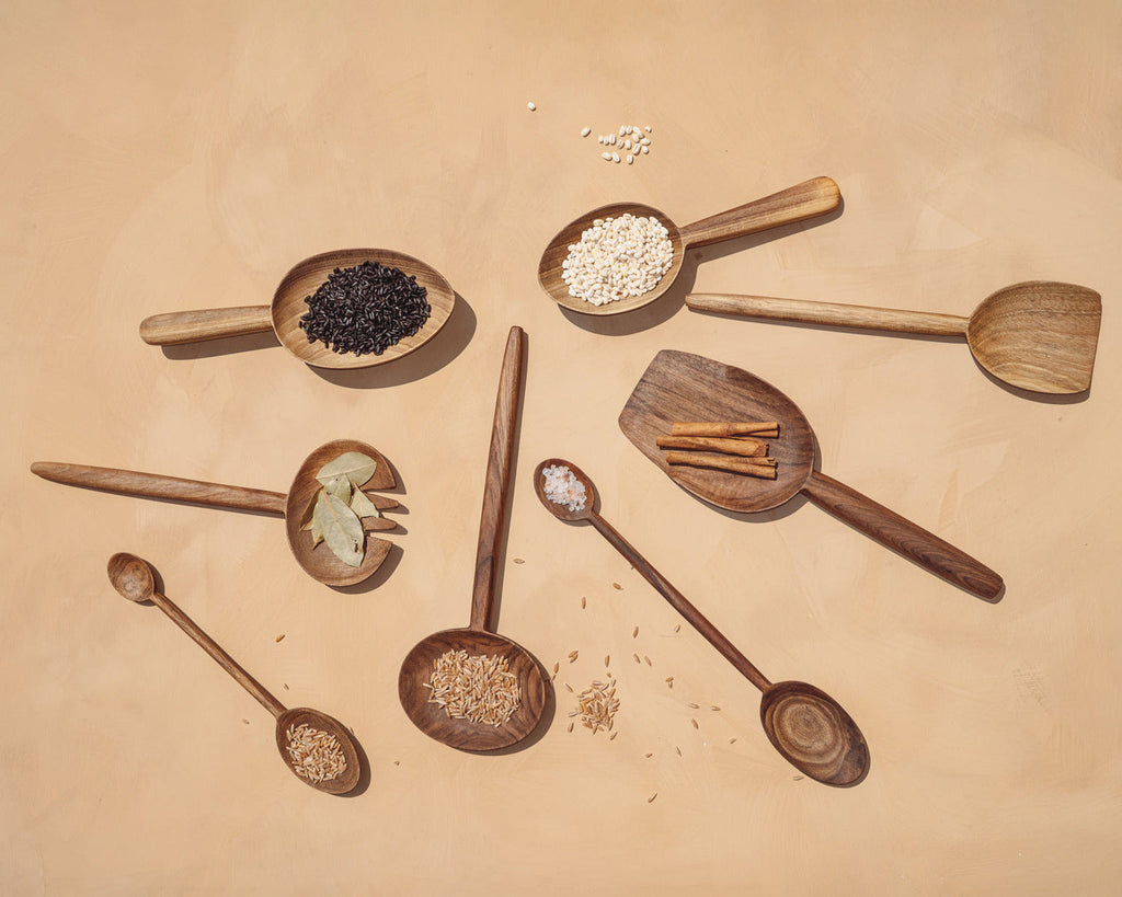Overhead spread of walnut spoons and serving pieces holding spices and grains on a warm sandstone surface