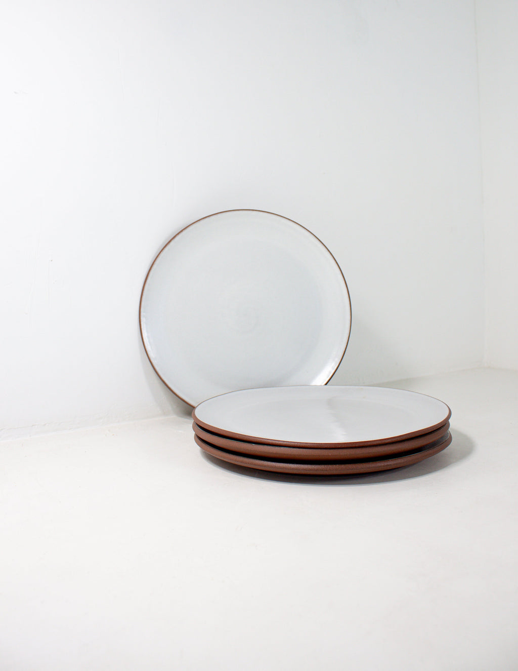 Hand-thrown stoneware coupe dinner plates in white glaze, one propped upright behind a stack of three