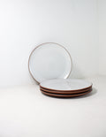 Hand-thrown stoneware coupe dinner plates in white glaze, one propped upright behind a stack of three