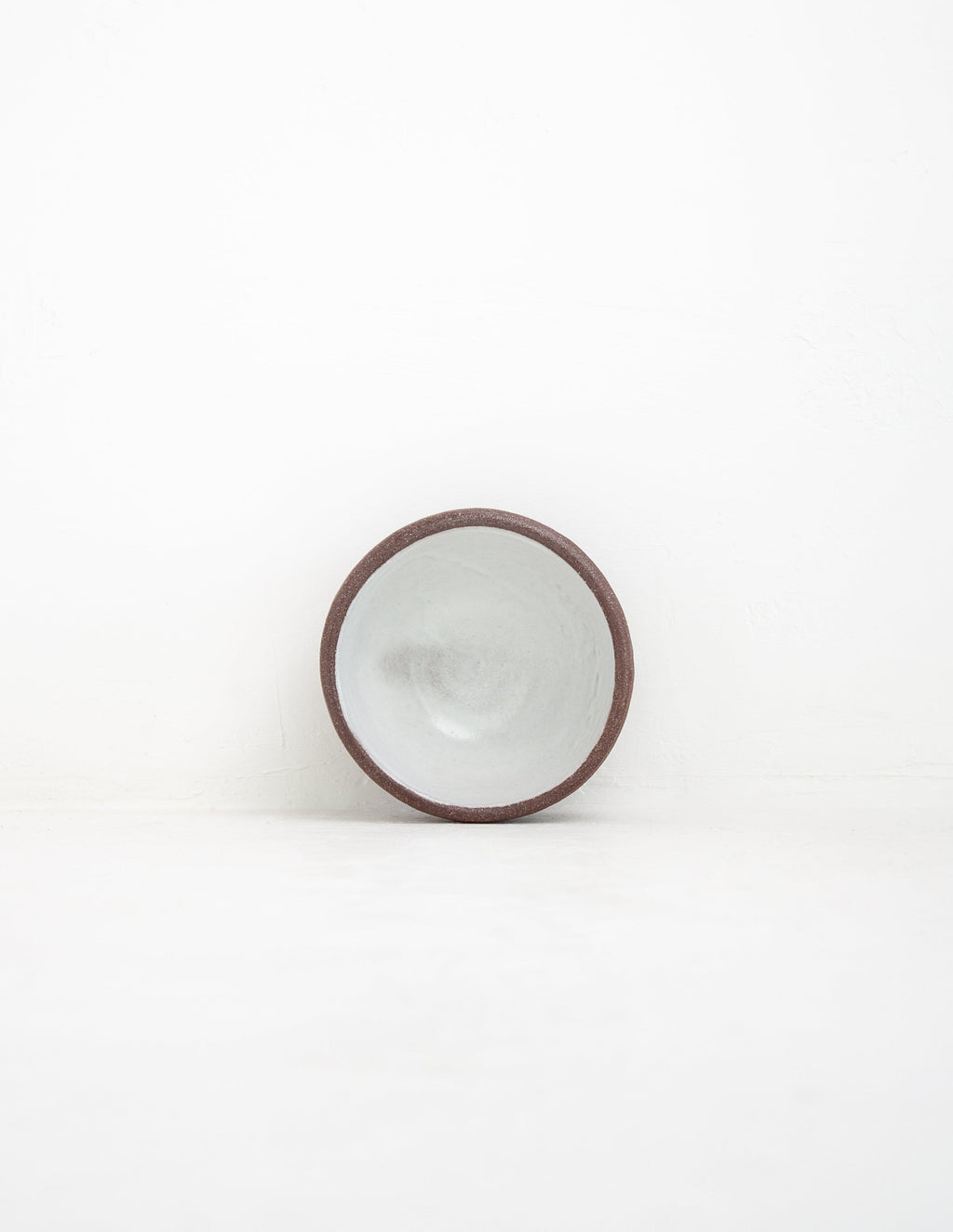 Hand-thrown stoneware coupe sauce bowl in white glaze tipped upright to show the interior and clay rim