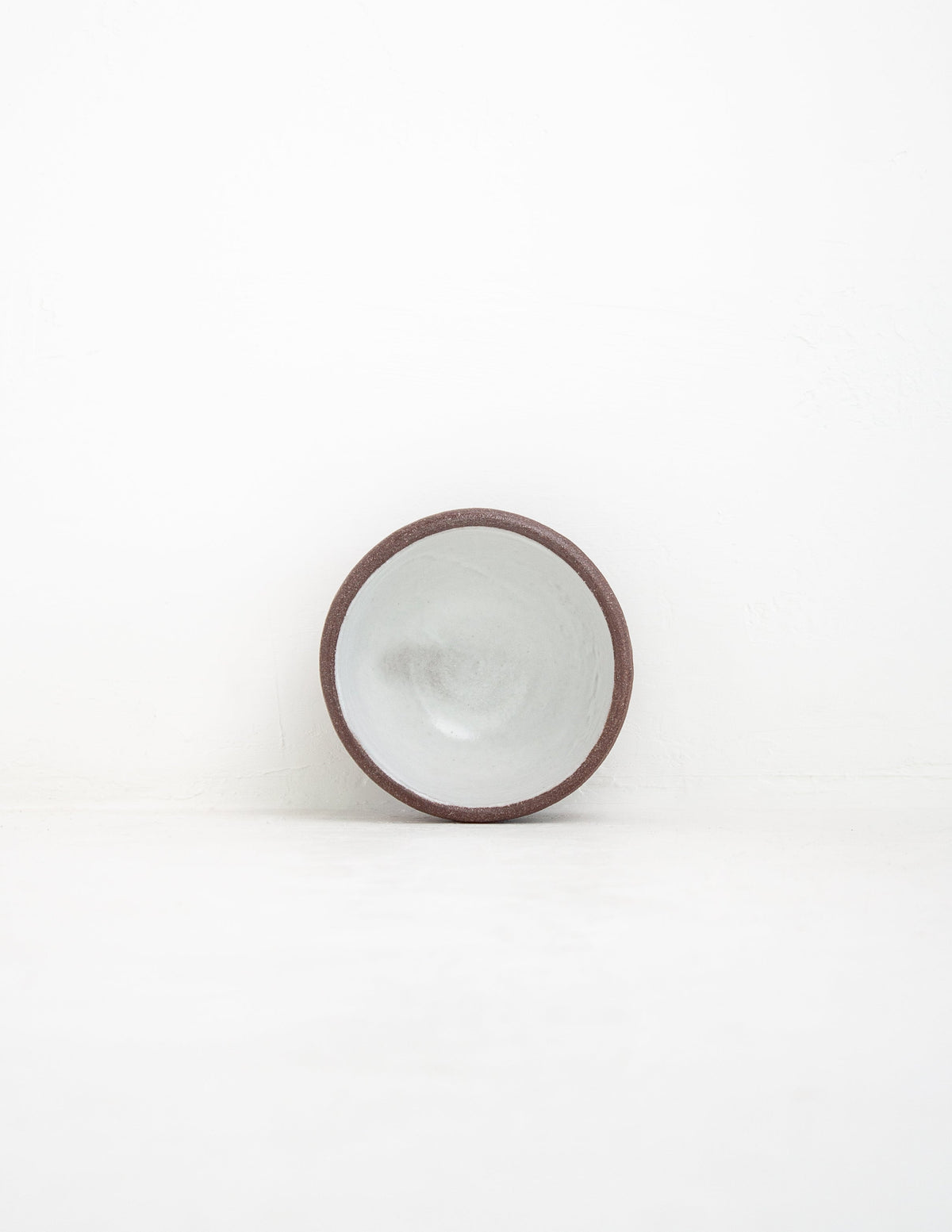 Hand-thrown stoneware coupe sauce bowl in white glaze tipped upright to show the interior and clay rim