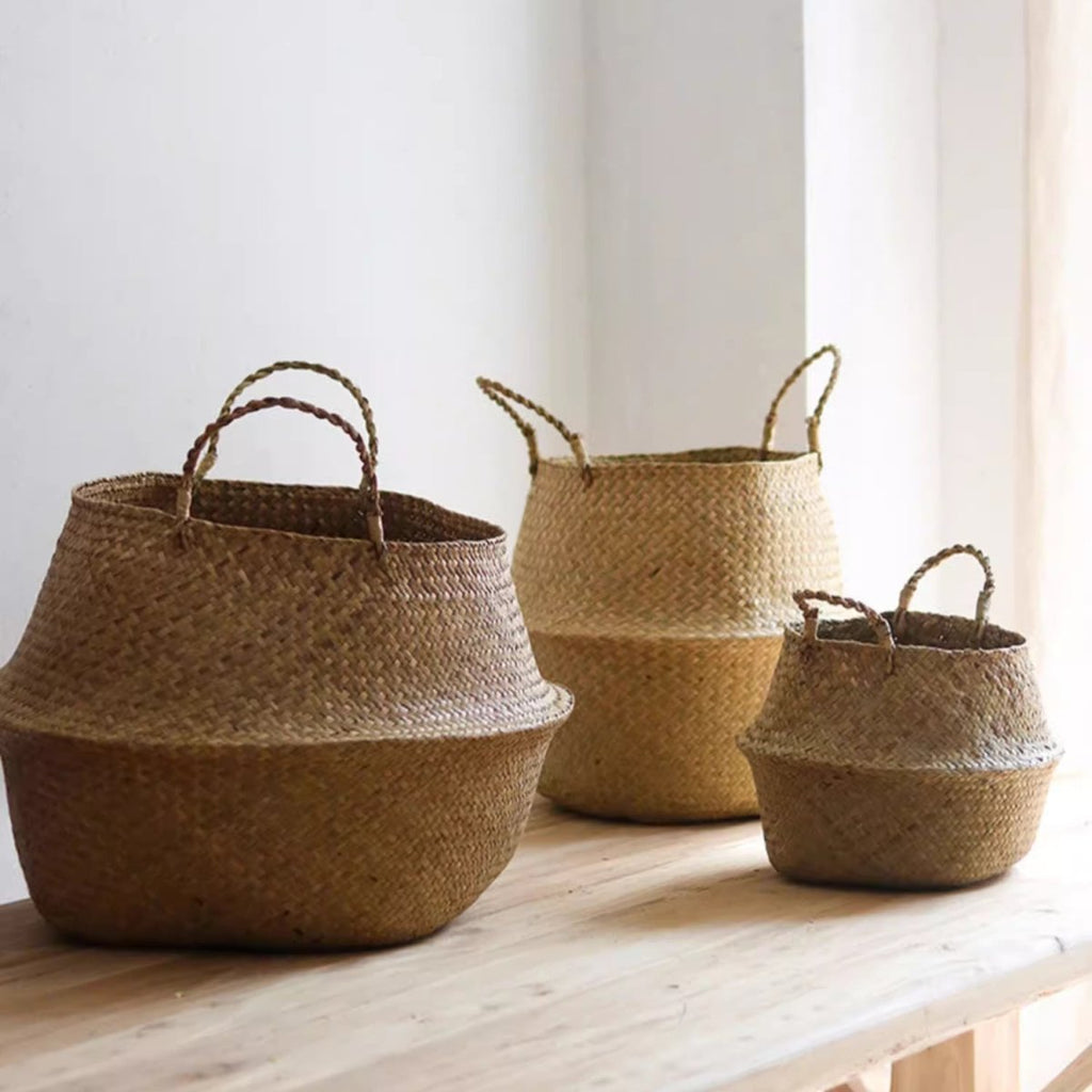 Large, medium and small woven seagrass belly baskets with twisted handles in a row on a pale wood table