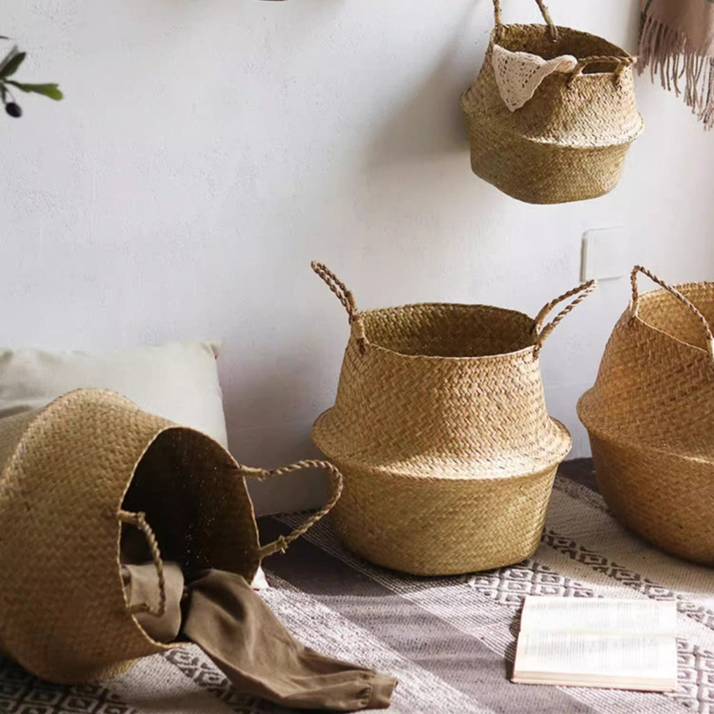 Seagrass belly baskets on a patterned rug, one tipped over with a folded cloth, one hung on the wall