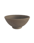 Large footed ceramic serving bowl in warm clay tone with carved vertical lines on a green background