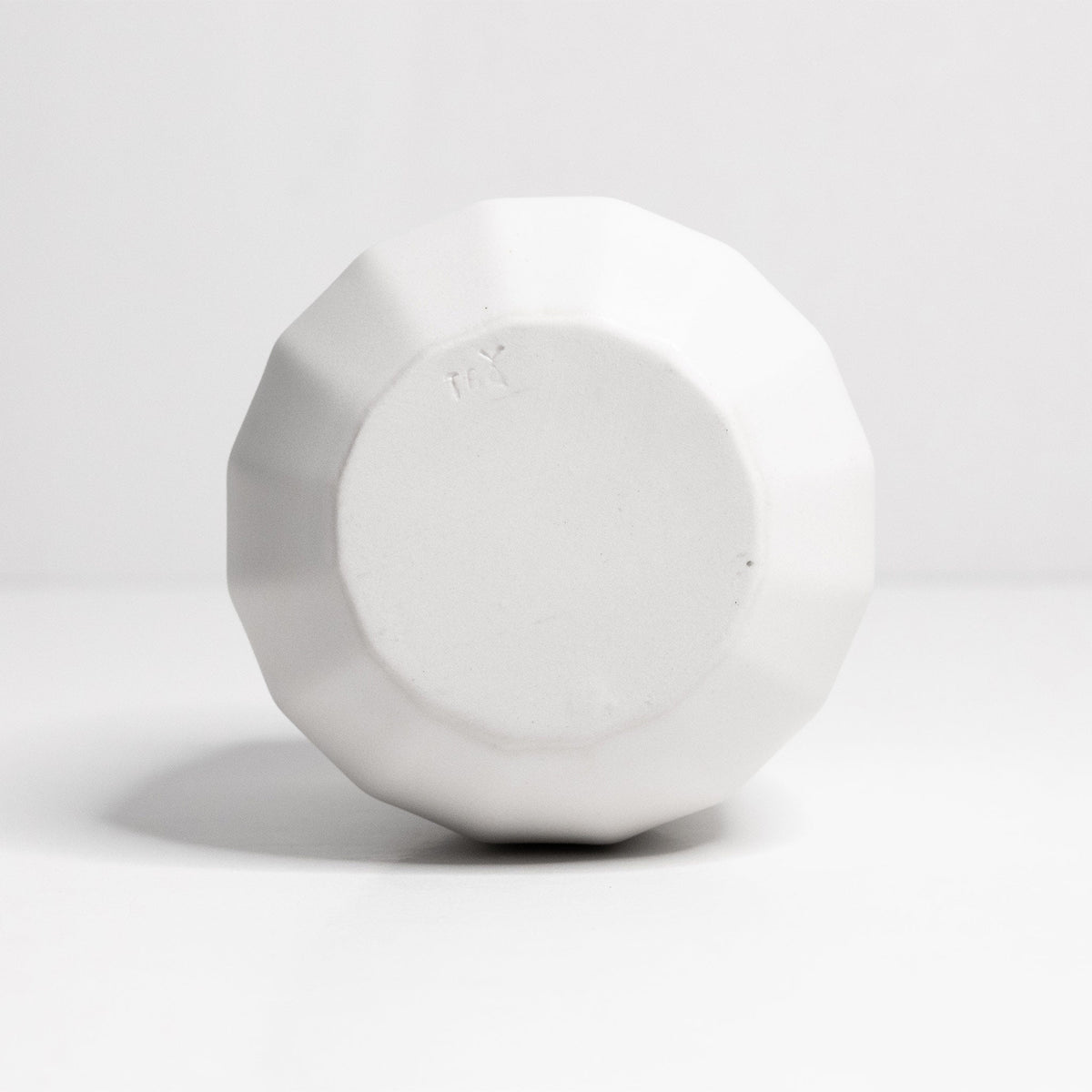 Underside of a white porcelain stemless wine glass showing the faceted body and unglazed base