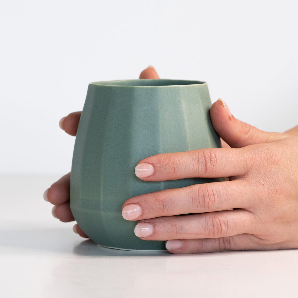 Hands wrapped around a Rosemary Green porcelain stemless wine glass to show its scale and easy grip