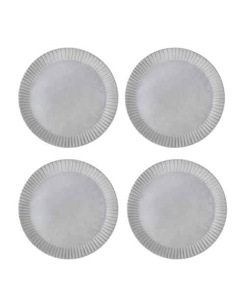 Four matte white ceramic dinner plates with hand-carved line rims, shown from above on a black ground
