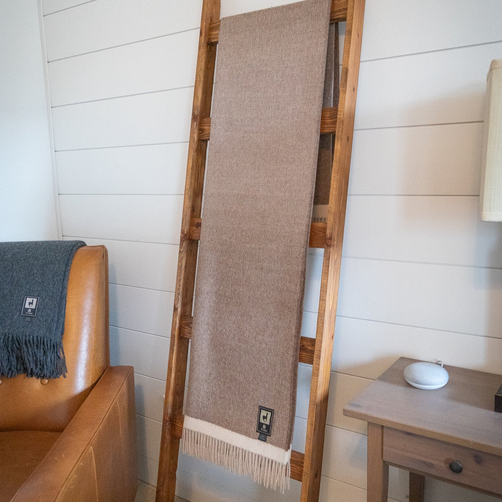 Brown baby alpaca throw on a leaning wooden ladder in a white paneled room next to a leather chair