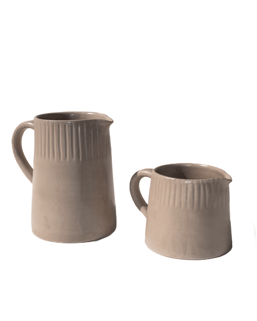 Two carved clay-toned ceramic pitchers in large and small sizes on a deep green background