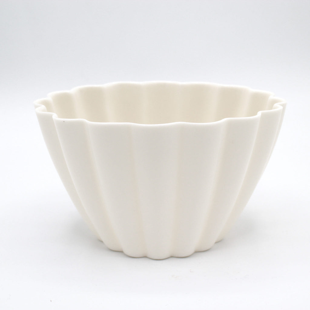 Fluted white porcelain candle holder on a white backdrop showing its ribbed sides and scalloped rim