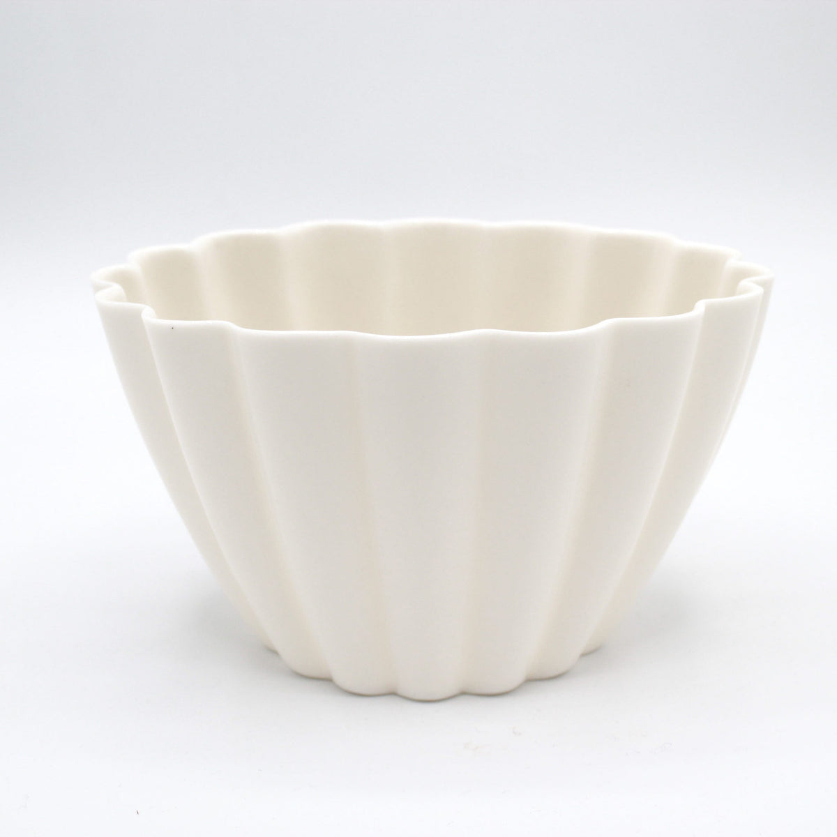 Fluted white porcelain candle holder on a white backdrop showing its ribbed sides and scalloped rim