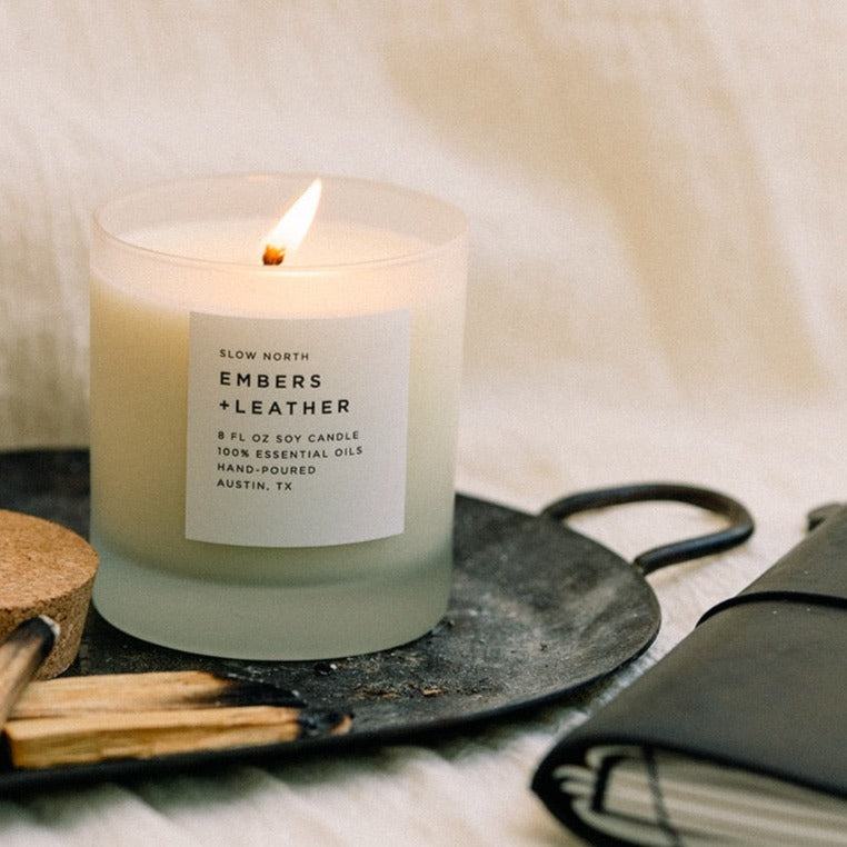 Lit frosted glass candle on a cast iron pan with wood spoons and a leather notebook on cream linen