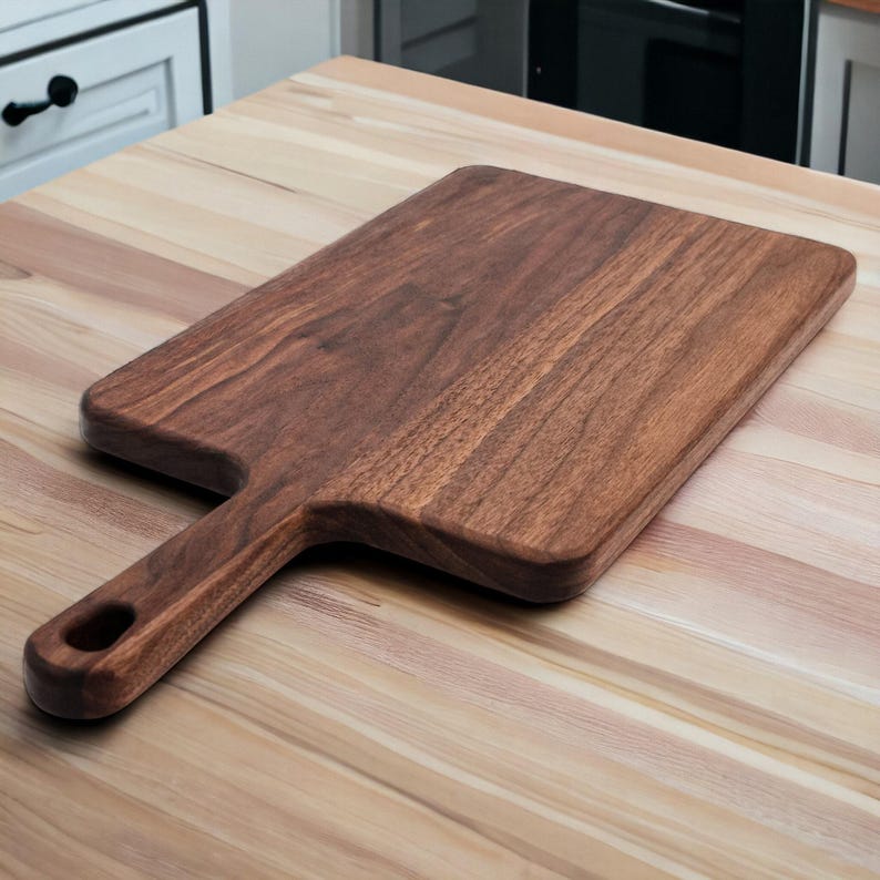 Wide walnut paddle serving board resting on a butcher block counter in a white kitchen