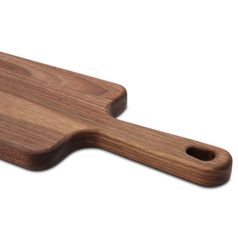 Close view of the handle and hanging hole on a narrow walnut paddle serving board on white