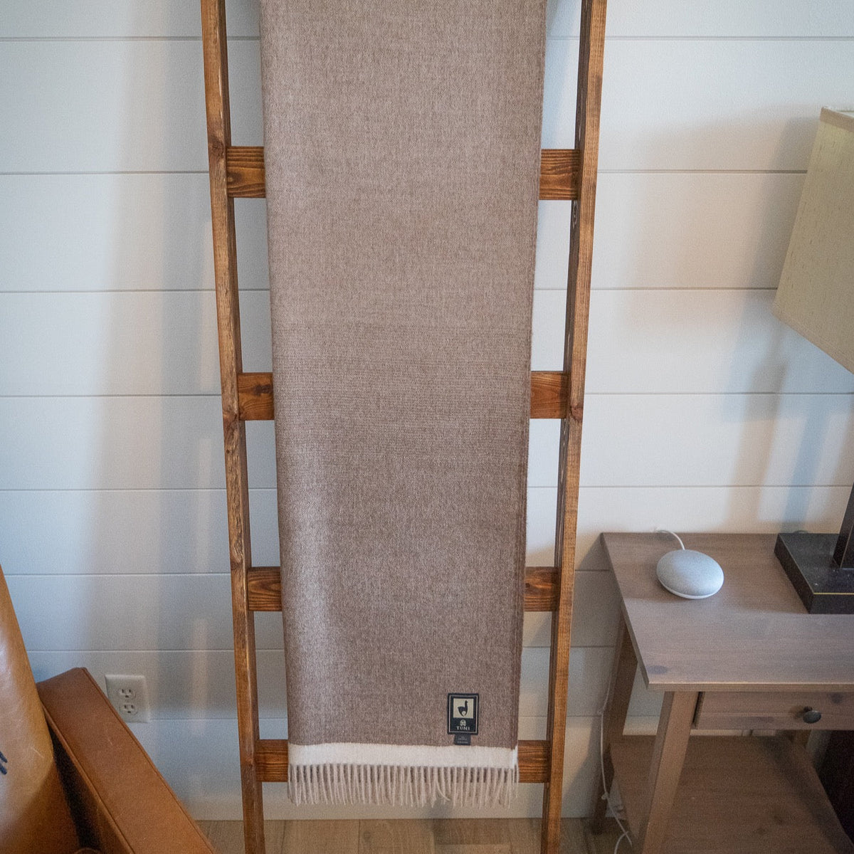 Brown baby alpaca herringbone throw hanging full length on a wooden blanket ladder beside a side table