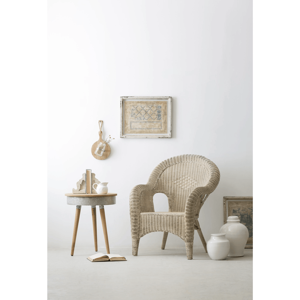 White terracotta jar on the floor beside a wicker chair and small side table in a pale room