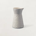 Matte pearl stoneware carafe with a gently dimpled, hand-shaped surface and pinched spout on a pale backdrop