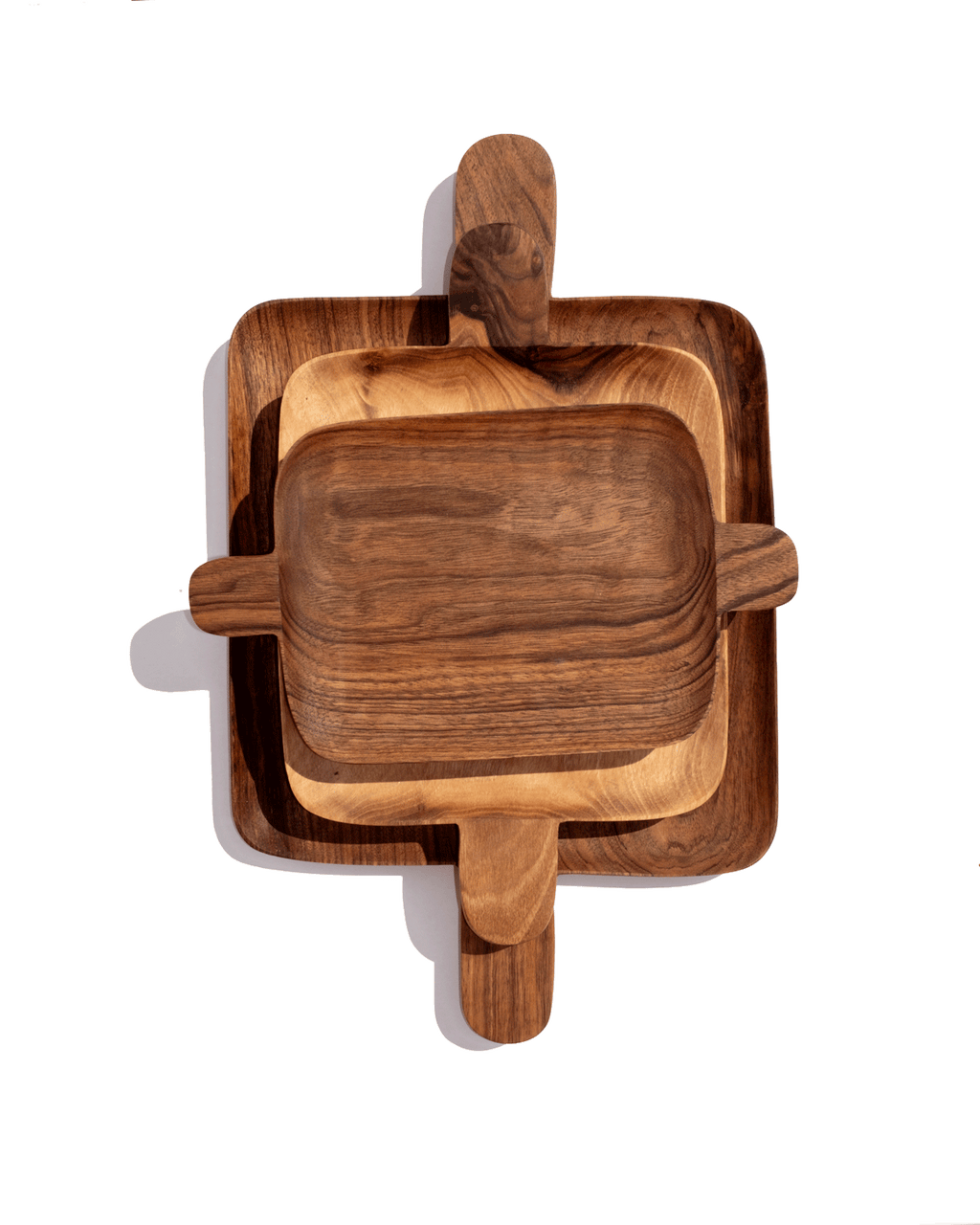 Three nested walnut serving trays with handles at each end, stacked from large to small on green
