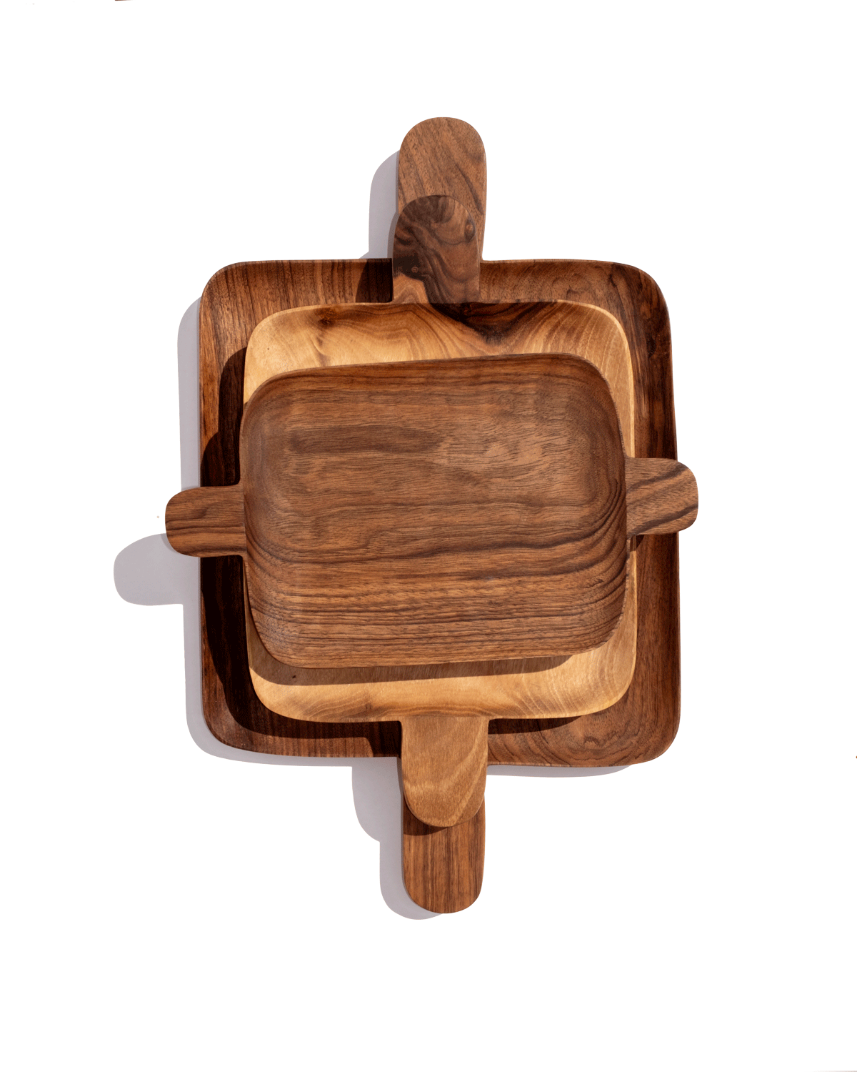 Three nested walnut serving trays with handles at each end, stacked from large to small on green