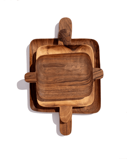 Three nested walnut serving trays with handles at each end, stacked from large to small on green