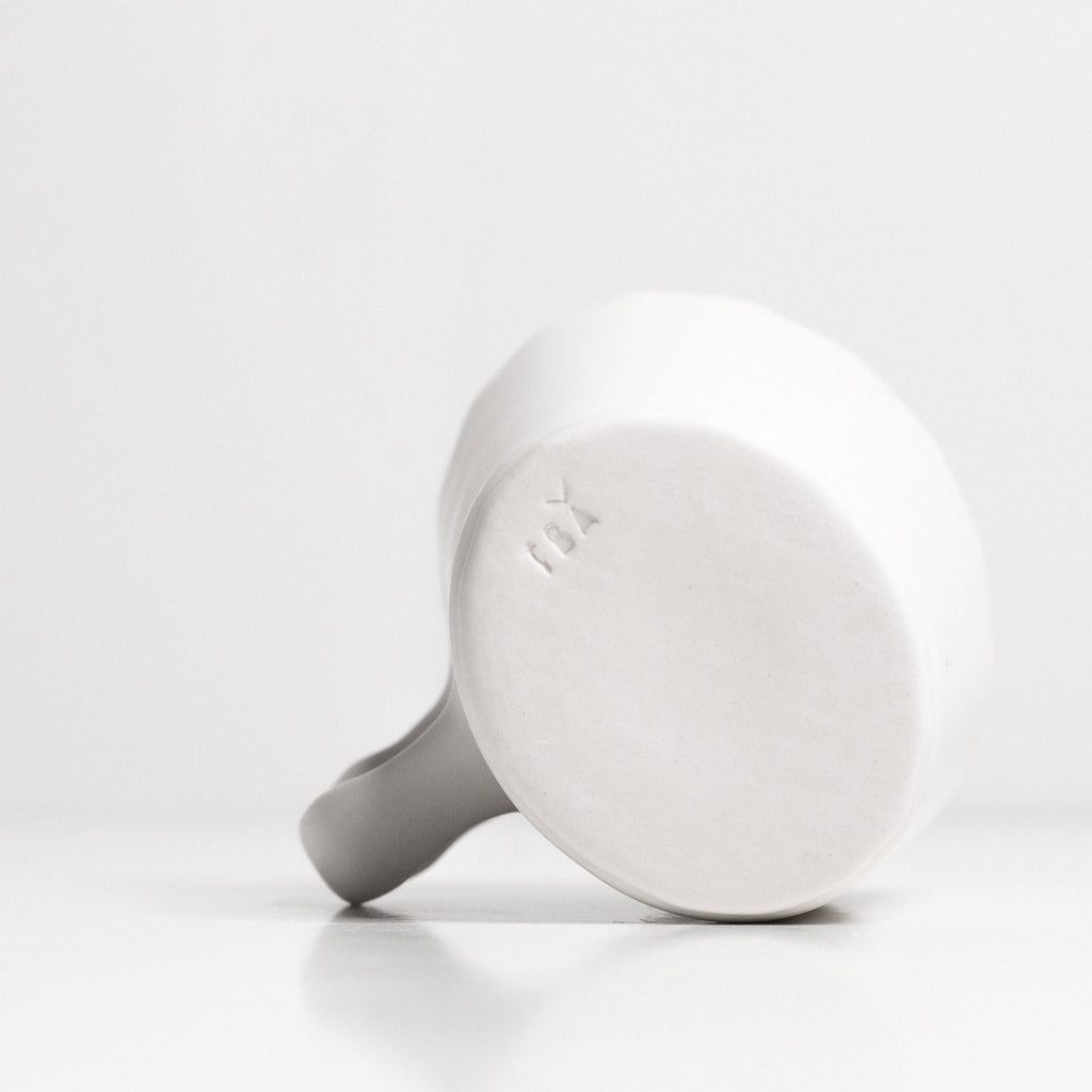 Underside of a white porcelain espresso cup showing its faceted walls, handle and unglazed base