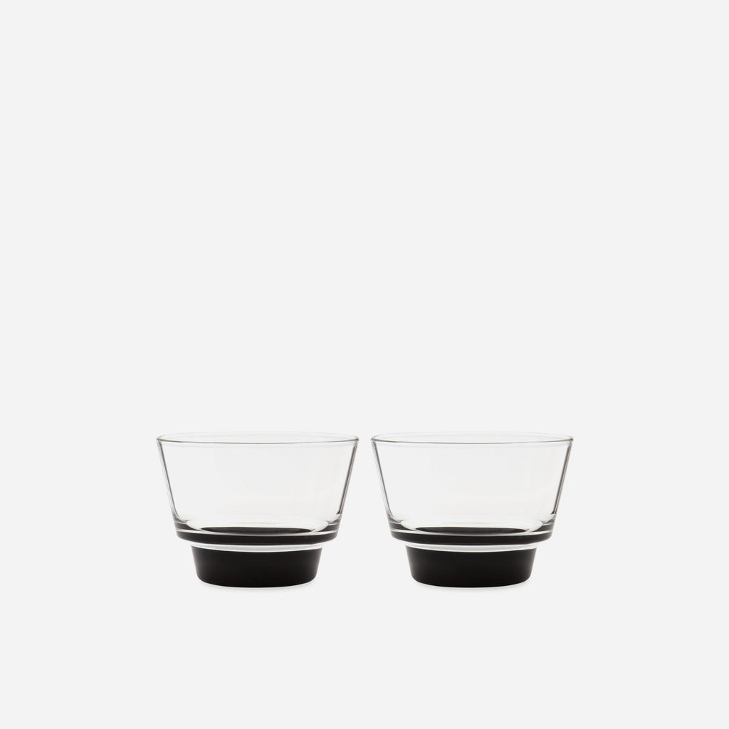 Pair of small handblown glass cups with flared clear bowls and solid black bases on a pale gray background