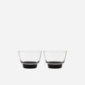 Pair of small handblown glass cups with flared clear bowls and solid black bases on a pale gray background