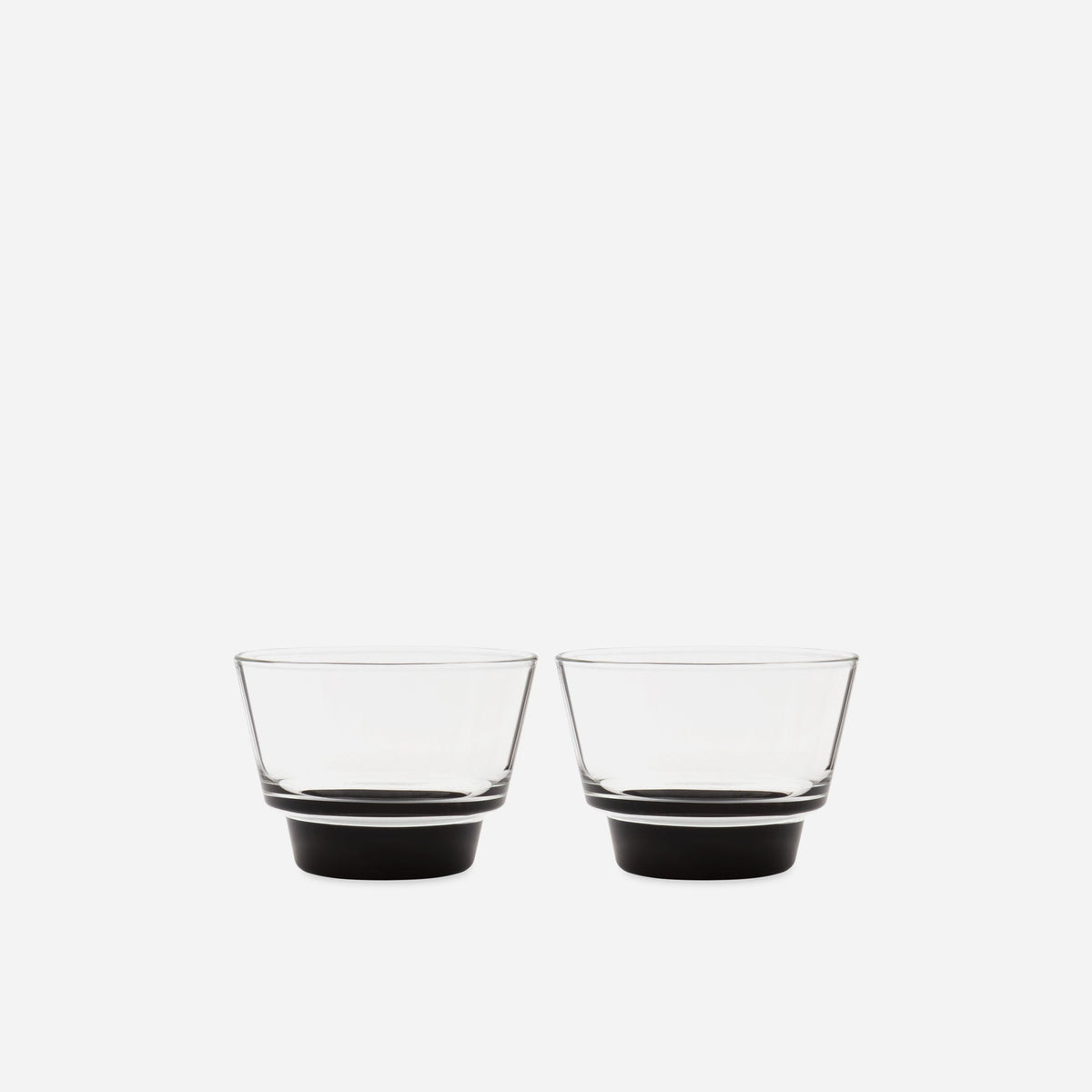 Pair of small handblown glass cups with flared clear bowls and solid black bases on a pale gray background