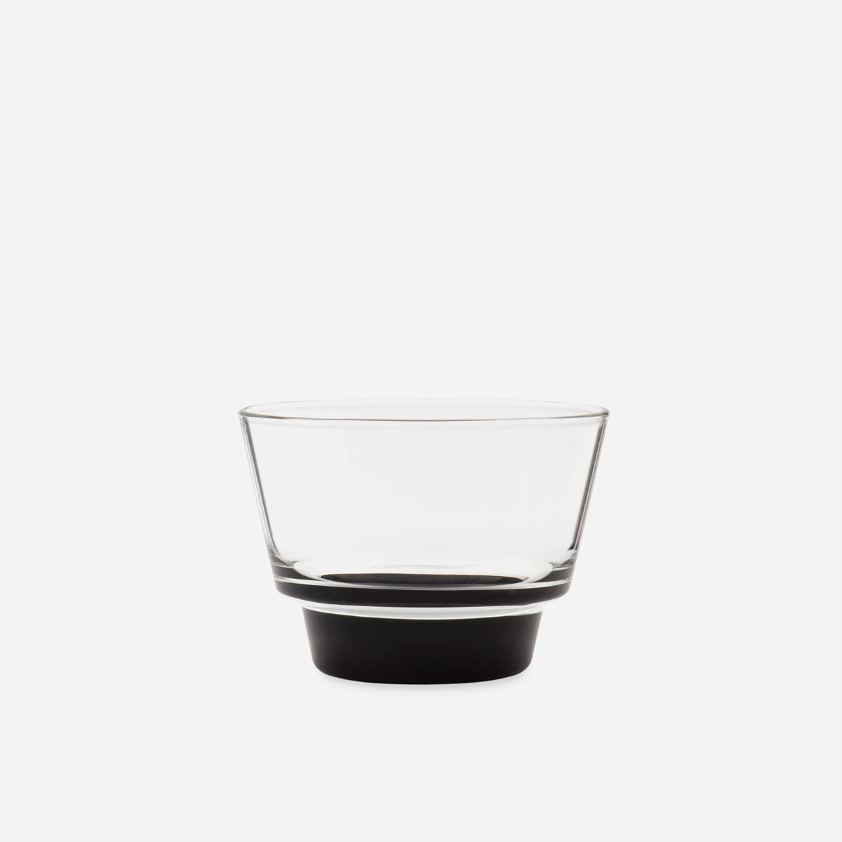 Close view of one small handblown glass cup with a flared clear bowl and a stepped black base on pale gray