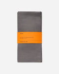 Folded slate gray linen napkin set wrapped with an orange paper band, shown on a pale gray background