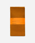 Folded turmeric orange linen napkin set wrapped with a printed paper band on a pale gray background