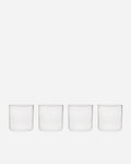 Four short handblown glass tumblers with straight sides and thin rims lined up on a pale grey background