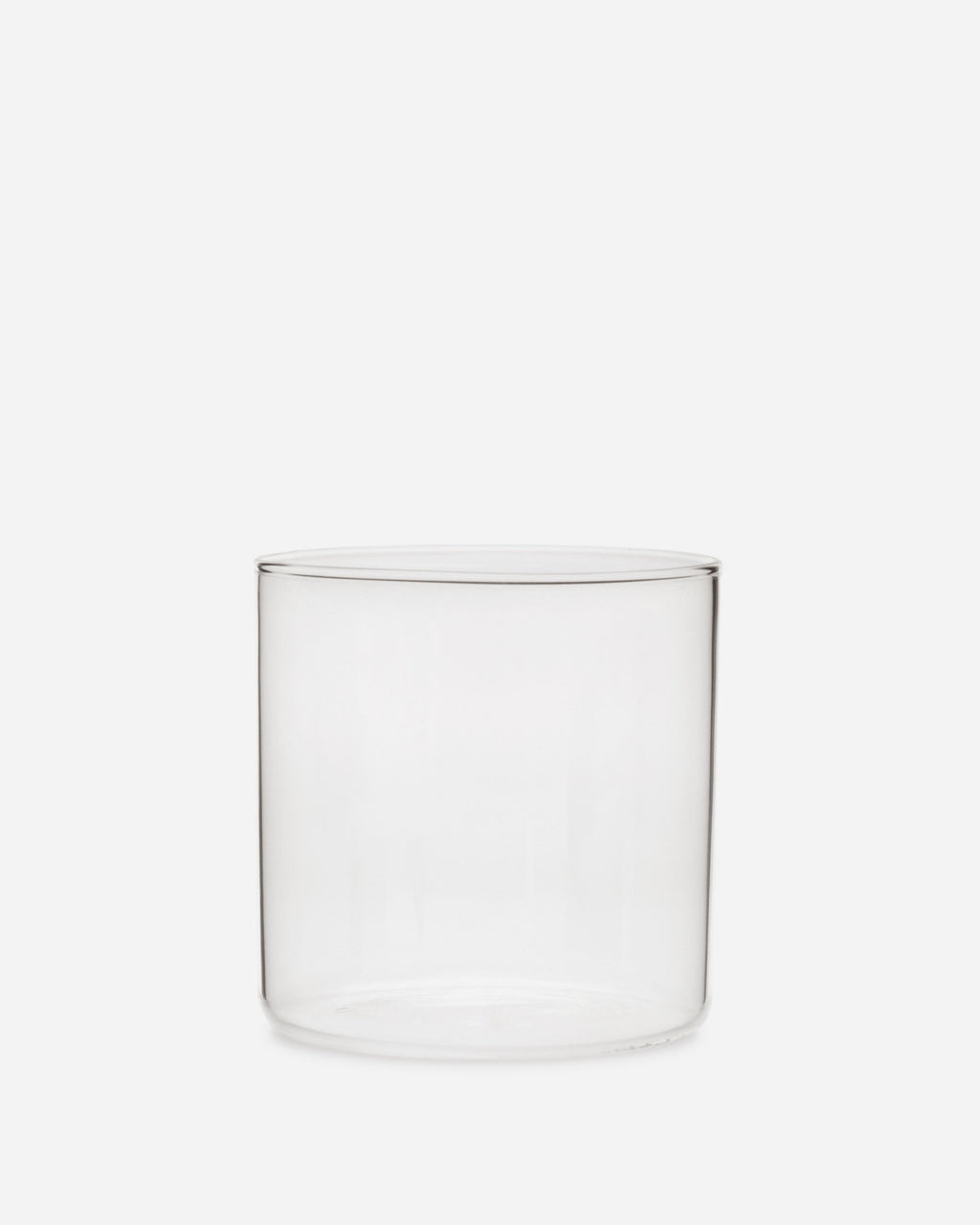 Single short handblown glass tumbler, a clean clear cylinder with a thin rim, shown on a pale grey background