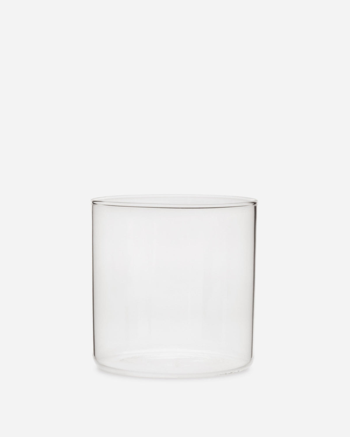 Single short handblown glass tumbler, a clean clear cylinder with a thin rim, shown on a pale grey background