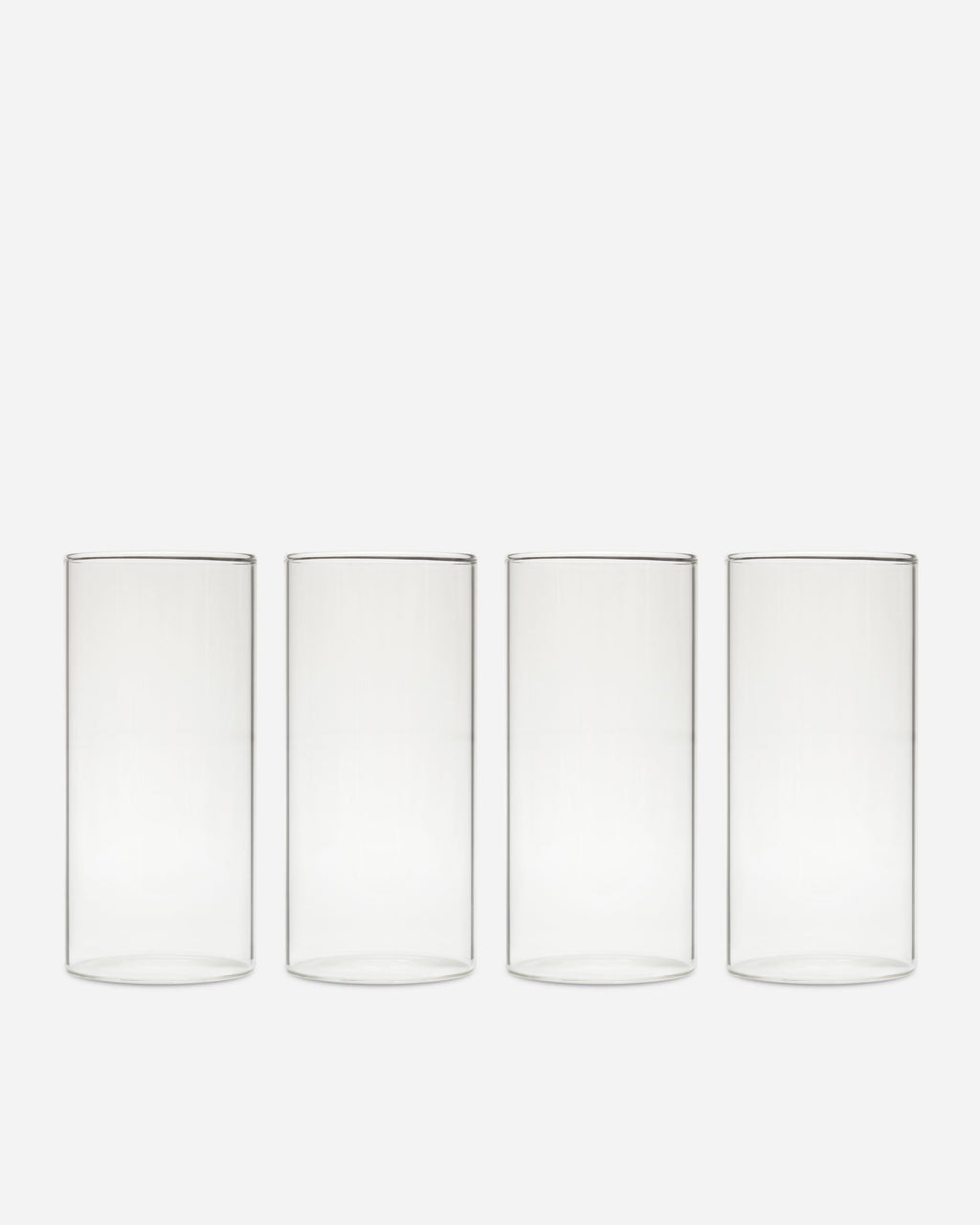 Four tall clear handblown drinking glasses lined up in a row on a pale gray background