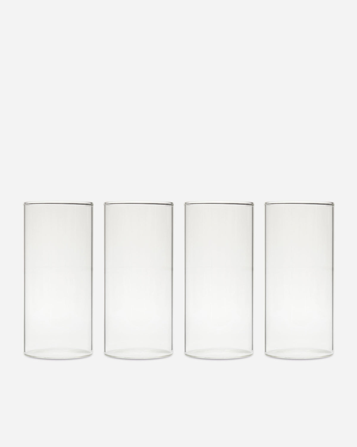 Four tall clear handblown drinking glasses lined up in a row on a pale gray background