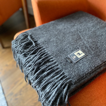 Charcoal alpaca wool blend throw with long fringe folded over the arm of an orange armchair