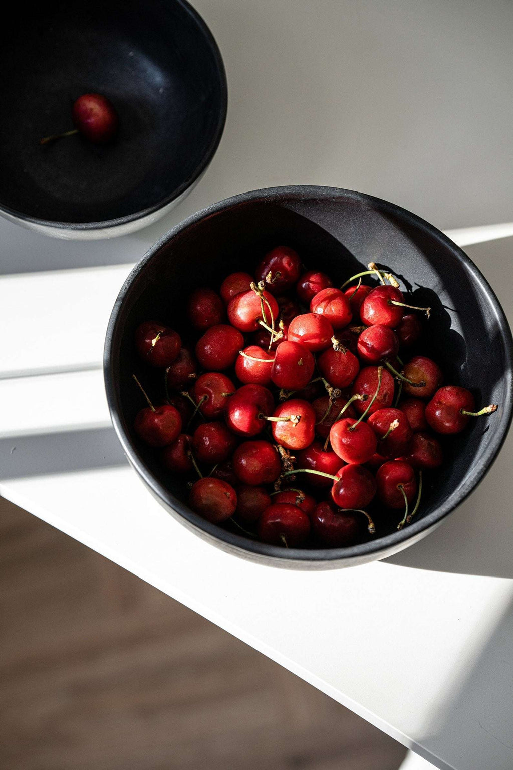 Matte black stoneware serving bowl filled with red cherry tomatoes on a white counter, seen from above