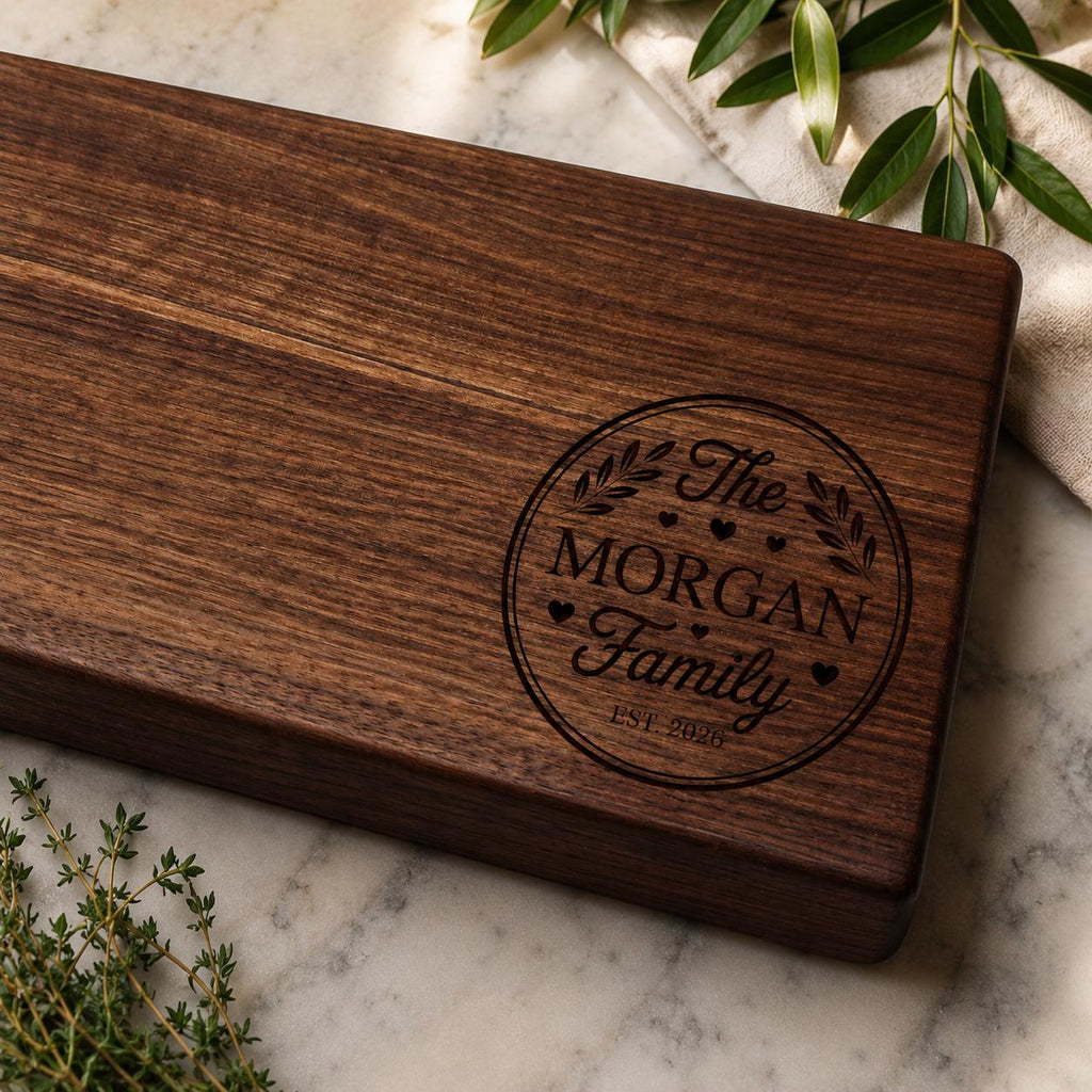 Walnut serving board corner with a sample family name engraving, shown on marble with herbs