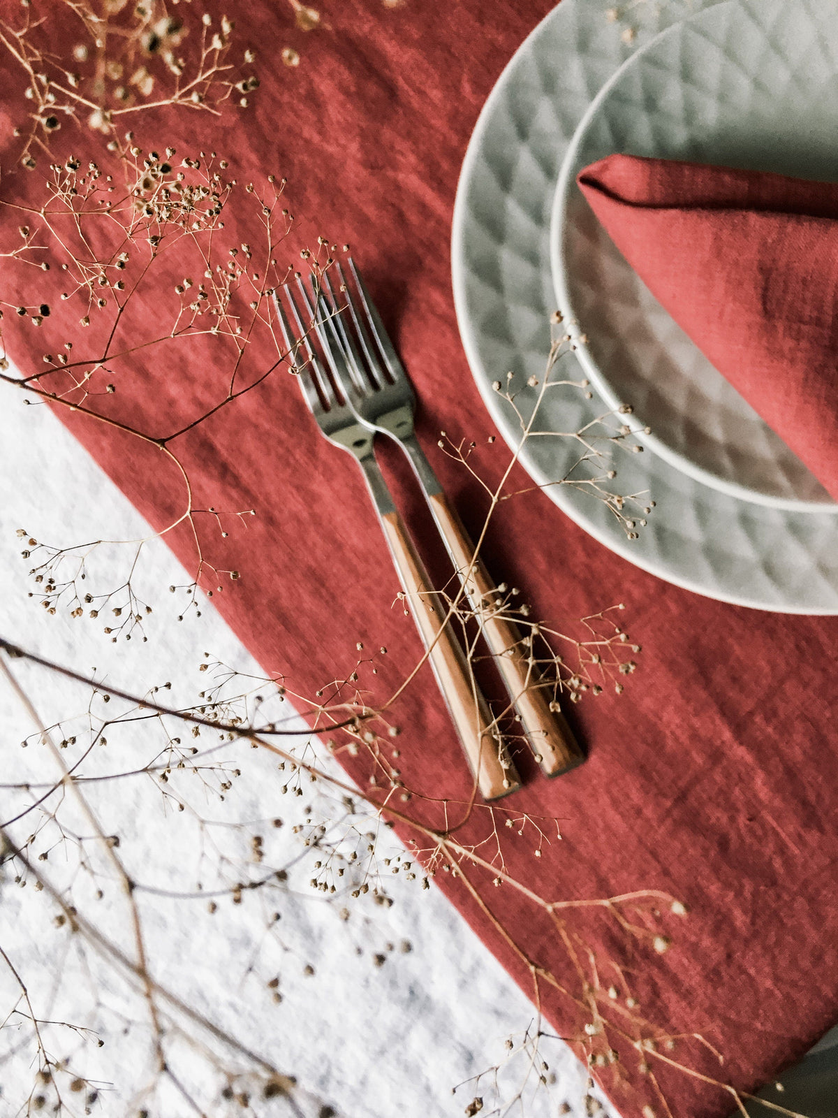 Russet linen table runner over white linen with a dark-handled fork and textured white ceramic plates